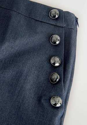 Denim nederdel i en mørkeblå stof, med en glat tekstur og fem blanke, dekorative knapper langs siden. Lynlås lukning bagpå.