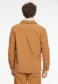 Bruine corduroy overhemdjas met een kraag, lange mouwen en geknoopte manchet, met een verticale ribbelstructuur en een relaxed fit.