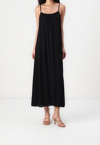 Černé maxi šaty s tenkými ramínky, lehkým materiálem, řaseným výstřihem a splývavou siluetou. V kombinaci s béžovými sandály na podpatku.