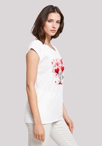 White short-sleeve t-shirt featuring a colorful heart tree graphic in red and pink with a black text detail at the base.