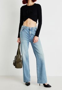 Zwarte lange mouwen crop top, lichtblauwe wijde jeans en zwarte puntige hakken. Olijfgroene schoudertas met meerdere vakken.