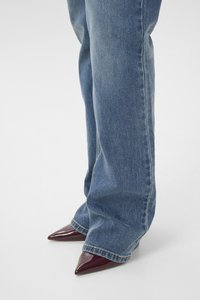 Pointed-toe burgundy heels paired with wide-leg blue jeans, featuring a faded denim texture and visible stitching along the seams.