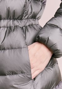 Šedá péřová bunda s hladkou, lesklou texturou, elastickými manžetami a boční kapsou. Stahovací pas na gumičku pro nastavitelný střih.