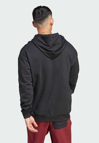 Sudadera negra con capucha hecha de una tela suave, con un corte relajado y puños acanalados. Sin logos ni patrones visibles. Vista desde la parte de atrás.