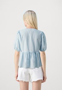 Top azzurro chiaro con maniche a sbuffo e vita arricciata. Realizzato in tessuto morbido, presenta un colletto rotondo e un orlo fluido, abbinato a pantaloni corti bianchi.