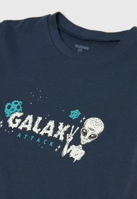 Námorně modré bavlněné tričko s grafickým designem, na kterém je text "GALAXY ATTACK", postava mimozemšťana, hvězdy a akcenty planet.