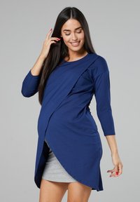 Navy blue maternity top with a diagonal wrap design, made from soft fabric. Features three-quarter sleeves and a relaxed fit.