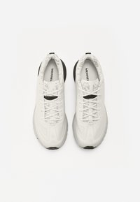 Baskets de sport blanches avec une tige en mesh texturé et une semelle en caoutchouc flexible. Présente des accents noirs contrastants au niveau du talon.