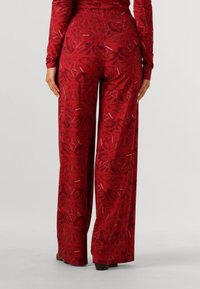 Pantalons larges à motifs rouges fabriqués en tissu doux, présentant un design floral avec un léger éclat et une taille élastique pour le confort.