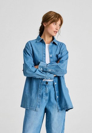 Svetlomodrá rifľová košeľa s gombíkovým zapínaním, dlhými rukávmi, predným vreckom a voľným strihom, v kombinácii s rifľovými nohavicami rovnakej farby. Hladká textúra.