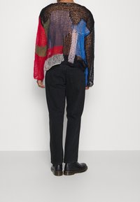 Translucent, multicolored knit sweater featuring red, blue, green, and black patches. Paired with black jeans and black ankle boots.