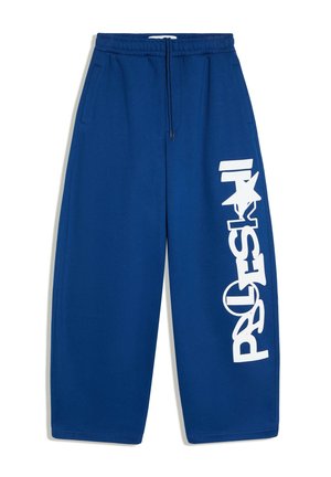 Pantalon de jogging bleu à jambes larges avec taille élastique, cordon de serrage, poches latérales et grand texte graphique blanc sur la jambe droite.