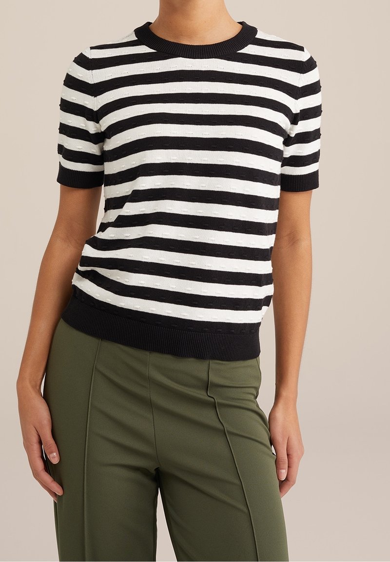 Svart- och vitrandig kortärmad topp med en ribbad rundhalsning och strukturerat tyg, kombinerad med gröna tapered byxor.