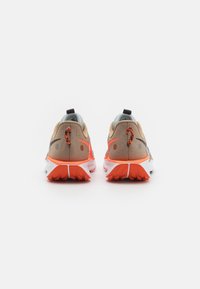 Un par de zapatillas deportivas en tonos beige y naranja vistas desde atrás sobre un fondo blanco, con suelas texturizadas y tiradores.