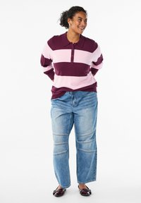 Un suéter a rayas color marrón y rosa con cuello y tres botones, combinado con jeans de pierna ancha en un tono azul claro que presentan detalles de costura.