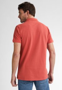Koraalkleurig polo-shirt met korte mouwen, klassieke kraag, zachte katoenen textuur en een rechte zoom, gecombineerd met blauwe jeans.