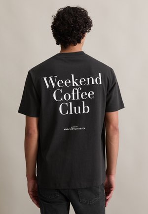 Black cotton t-shirt with short sleeves features large white text on the back: "Weekend Coffee Club" with "hosted by Marc O'Polo Denim."