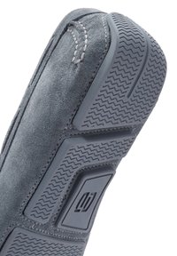 Grijze suède schoen met een rubberen zool met textuur, voorzien van een zigzagpatroon en een rechthoekige accent. Stiksels zichtbaar langs de randen.