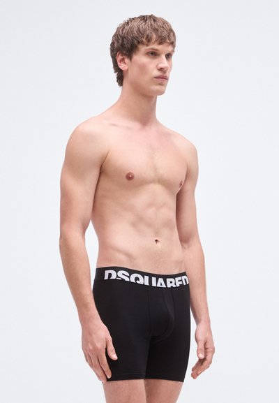 Črne boksarske kratke hlače z belim logotipom "DSQUARED" na pasu, izdelane iz gladkega materiala, s prileganim krojem in kratkimi hlačnicami.