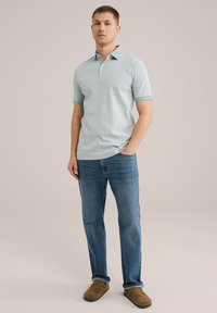 Cămașă polo cu model de culoare albastru deschis, cu guler și plastron cu nasturi, purtată cu blugi albaștri și pantofi slip-on maro.