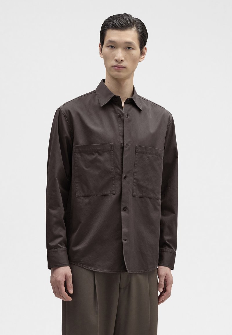 Brun langærmet skjorte lavet af stof med en glat tekstur, der har to forlommer og en krave, knaplukning og en afslappet pasform.