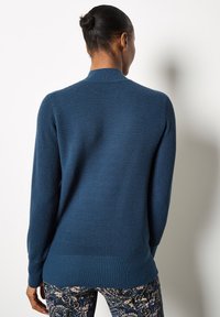 Sweter dzianinowy w głębokim niebieskim kolorze z prążkowaną teksturą i okrągłym dekoltem. Posiada długie rękawy oraz luźny krój. Zestawiony z wzorzystymi spodniami.