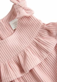Jasnoróżowy materiał w prążki z falbankami i detalem w postaci węzła przy dekolcie. Zawiera metkę z napisem "NEXT baby". Teksturowana powierzchnia.