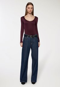 Body a maniche lunghe bordeaux abbinato a jeans in denim blu scuro a vita alta e una cintura nera con fibbia decorativa.