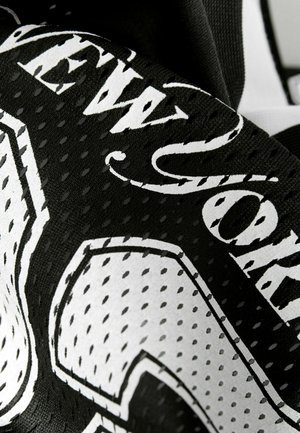 Suurendatud musta ja valge perforatsiooniga kangas, millel on stiliseeritud tekst ja graafilised detailid rõival või aksessuaaril.