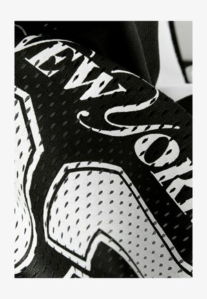 Nahaufnahme von schwarz-weißer durchbrochener Stoff mit stilisiertem Text und grafischen Details auf einem Kleidungsstück oder Accessoire.