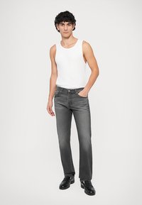 Pilki džinsai su tiesiu kirpimu, derinami su balta tankų. Minimalūs siuvimo elementai ir paprasti metaliniai aksesuarai. Juodi batai užbaigia įvaizdį.