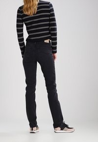 Pantalones vaqueros de denim negro con un corte ajustado, que presentan un diseño clásico de bolsillo trasero y una etiqueta de Lee en la cinturilla. Llevados con una blusa a rayas.