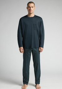 Dunkelblaues Langarm-Pyjama-Oberteil mit einer Brusttasche, kombiniert mit gestreiften Pyjama-Hosen in Dunkelblau mit hellblauen vertikalen Streifen.