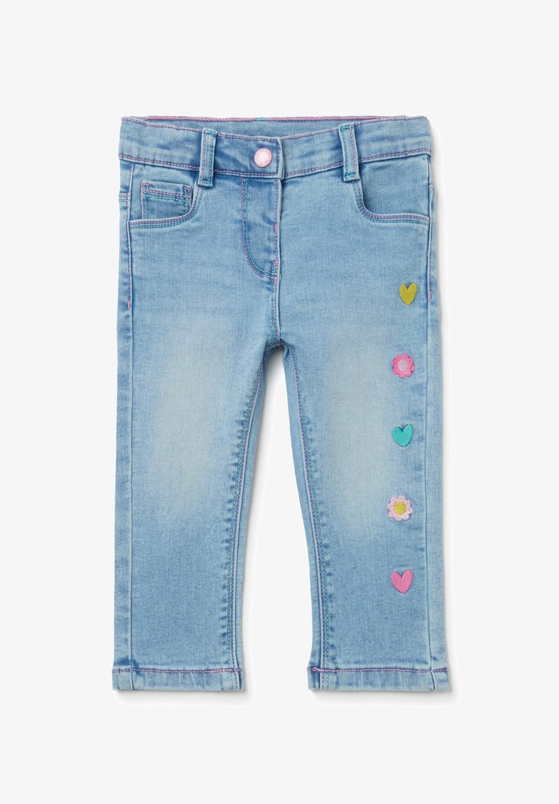 Pantalon en denim bleu clair avec une finition délavée, présentant des appliqués colorés de fleurs et de cœurs le long de la jambe gauche et des accents de couture rose.