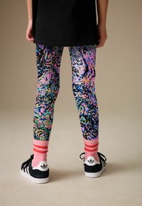 Colanți colorați cu bază neagră, având modele abstracte multicolore. Asortați cu adidași negri și șosete roz cu dungi.