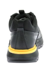 Zapatilla deportiva negra con parte superior de malla, suela de goma resistente y un acento amarillo distintivo alrededor de la mediasuela para mayor soporte.