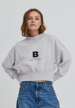 Sudadera gris corta con cuello alto, que presenta un logo negro de "B" y el texto "ORIGINAL BALL THE JEANS". Tela suave y ajuste relajado.