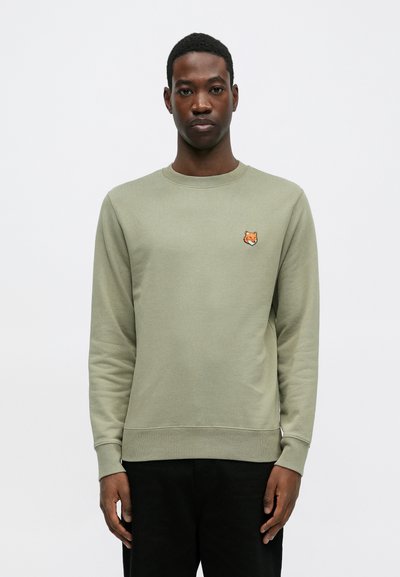Sweatshirt w kolorze oliwkowym z długimi rękawami, ściągaczami u dołu i przy rękawach. Posiada mały haftowany emblemat lisa na piersi. Wykonany z miękkiego materiału.