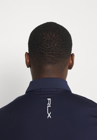 Marinblå polo skjorta med en mjuk textur, försedd med en vikbar krage och den vita "RLX"-logotypen på baksidan av nacken.