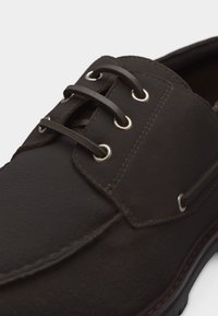 Σκούρο καφέ δερμάτινο παπούτσι με δερμάτινα κορδόνια που περνούν μέσα από μεταλλικά ρουμπάκια, λεπτομερείς ραφές και λείο στρογγυλεμένο σχέδιο μύτης.