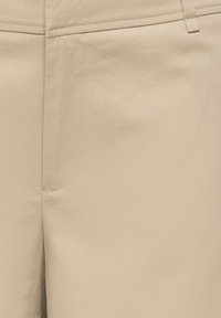 Pantalon beige avec une texture lisse, coupe droite et un détail de couture subtil près de la poche.
