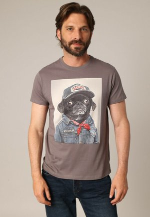 T-shirt en coton gris avec un graphique d'un carlin portant une veste en denim, une casquette et un bandana rouge, avec le texte "RUG & REPAIR".