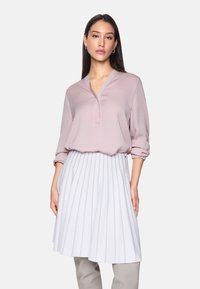 Light pink blouse with a V-neck and full sleeves, paired with a white pleated skirt featuring metallic accents and a flared silhouette.