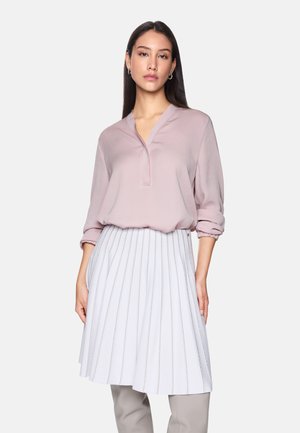 Lichtroze blouse met een V-hals en lange mouwen, gecombineerd met een witte geplooide rok met metallic accenten en een uitlopende snit.