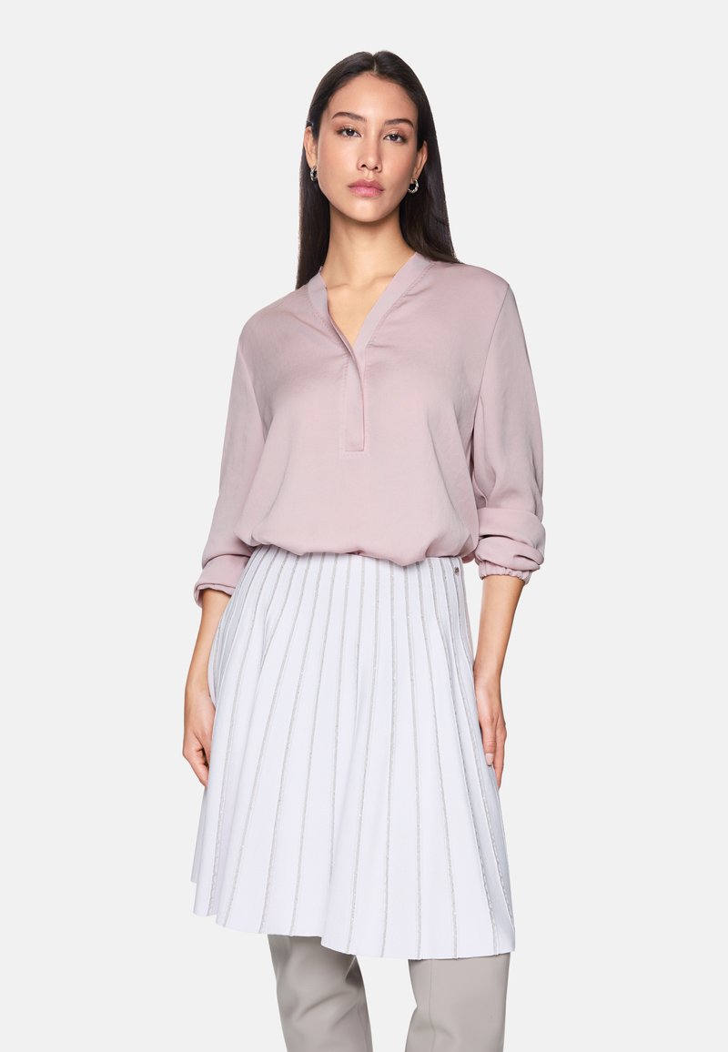 Light pink blouse with a V-neck and full sleeves, paired with a white pleated skirt featuring metallic accents and a flared silhouette.
