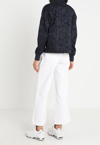 Námořnická oversized bunda s texturovaným vzorem, kombinovaná s bílými kalhotami s širokými nohavicemi a bílými teniskami. Má vysoký límec a elastické manžety.