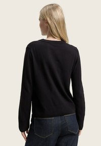 Pull noir à manches longues avec un col et des poignets côtelés, design ajusté et texture lisse, associé à un jean bleu foncé.