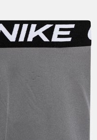 Halli spordirõivad musta vöökohtaga, millel on valge "NIKE" brändi logo. Materjal on siledaks viimistletud ja veidi läikiv, sobitav disain.