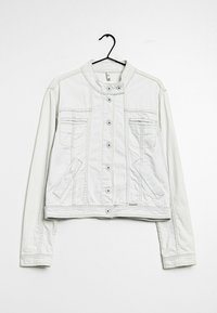 Bílá džínová bunda s knoflíkovým zapínáním, stojatým límcem, hrudními a bočními kapsami, zavěšená na černém ramínku na bílém pozadí.