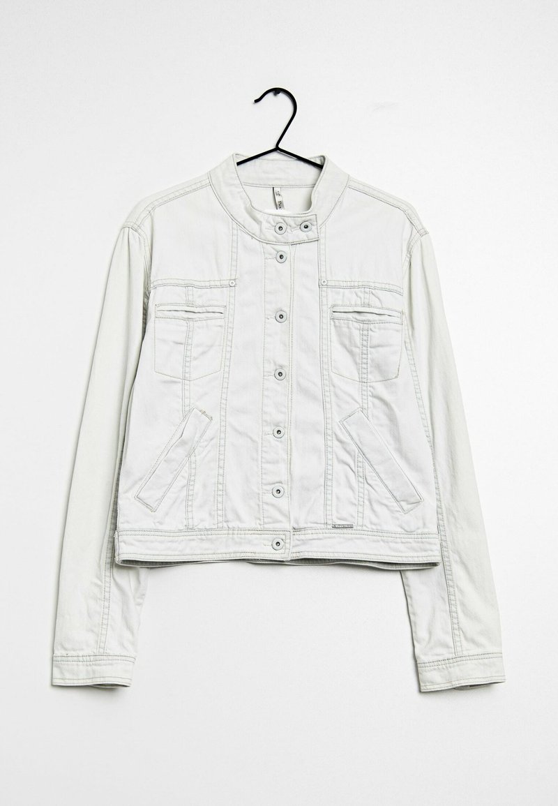 Bílá džínová bunda s knoflíkovým zapínáním, stojatým límcem, hrudními a bočními kapsami, zavěšená na černém ramínku na bílém pozadí.
